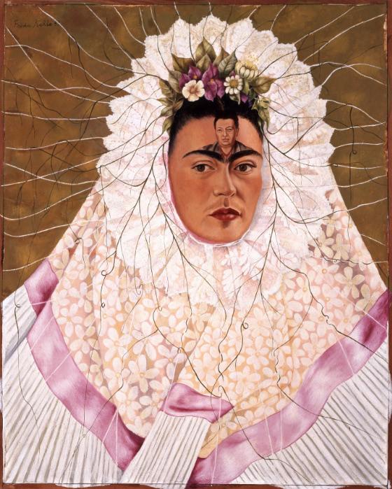 Portrait of Kahlo wearing a light-colored headdress that encircles her face. Above her brow is a small portrait of Rivera and flowers along her hairline.