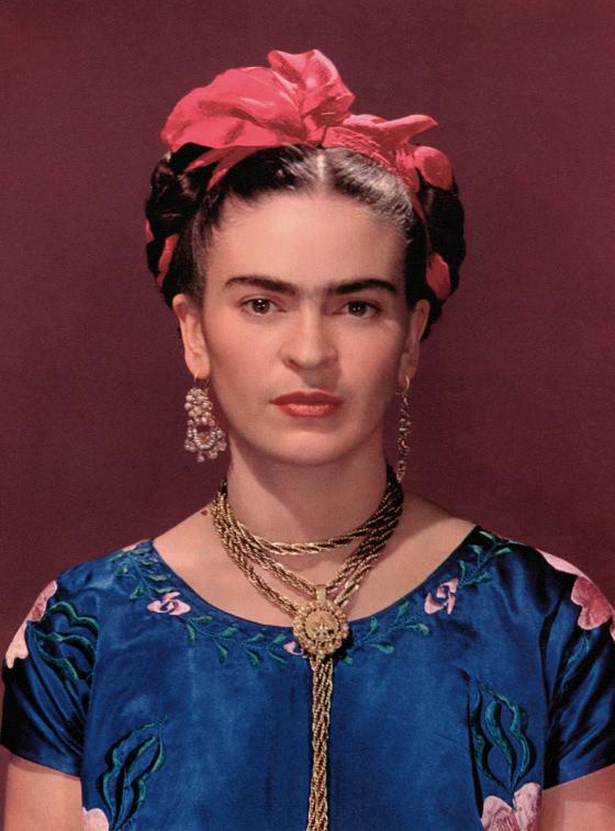 Color portrait of Kahlo in a blue blouse set against a deep red background. She wears large earrings and a braided gold necklace.