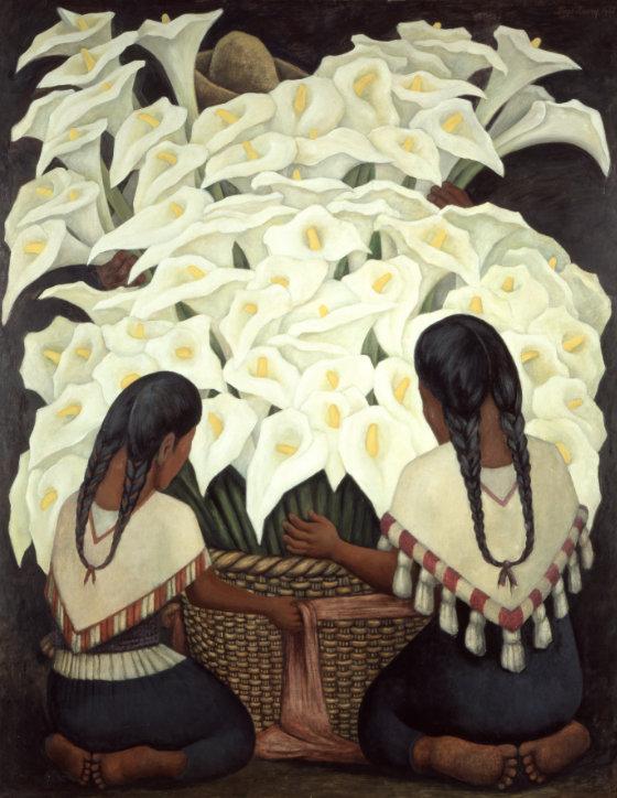 Two young women, on their knees, kneel before an oversized basket of white calla lilies. Barely seen behind the flowers, a flower vendor is visible only by his hat and his hands