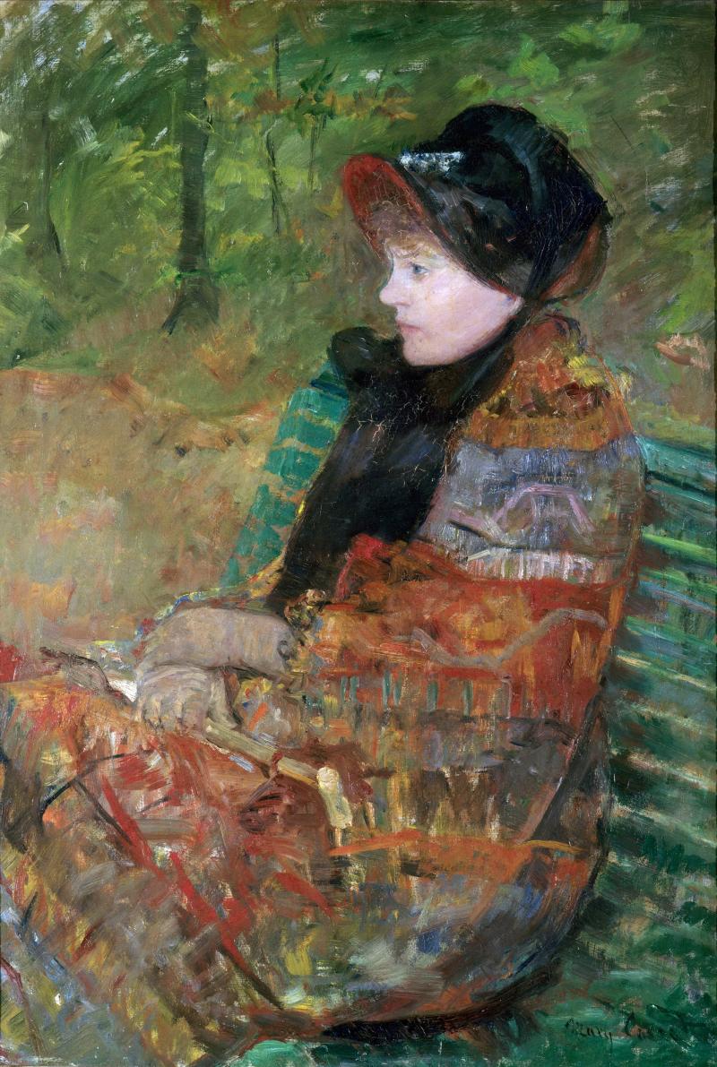 Una mujer con tapado y ropa abrigada sentada en un banco de un parque