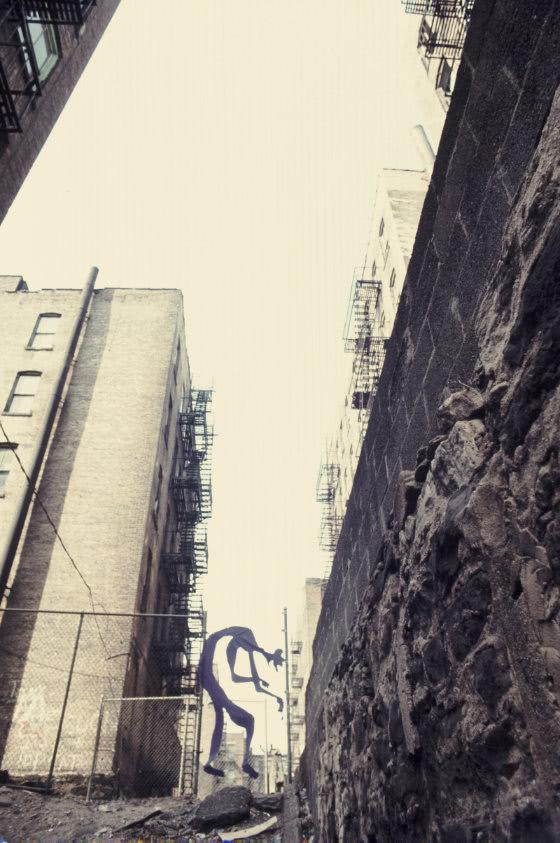 Photograph of large figure made of thin purple flag fabric hung in a street alleyway.