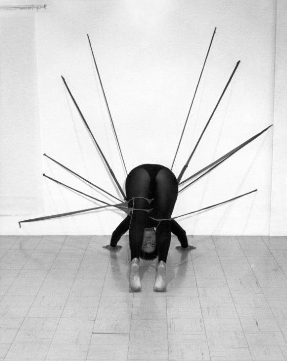 Black and white photograph showing a woman on the floor, dressed in black, moving while entangled in a web of nylon pantyhose.