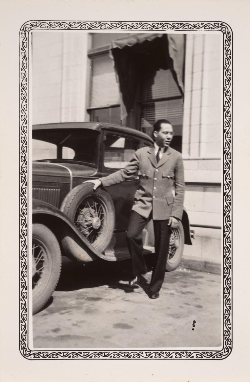 a man in a suit poses near a car