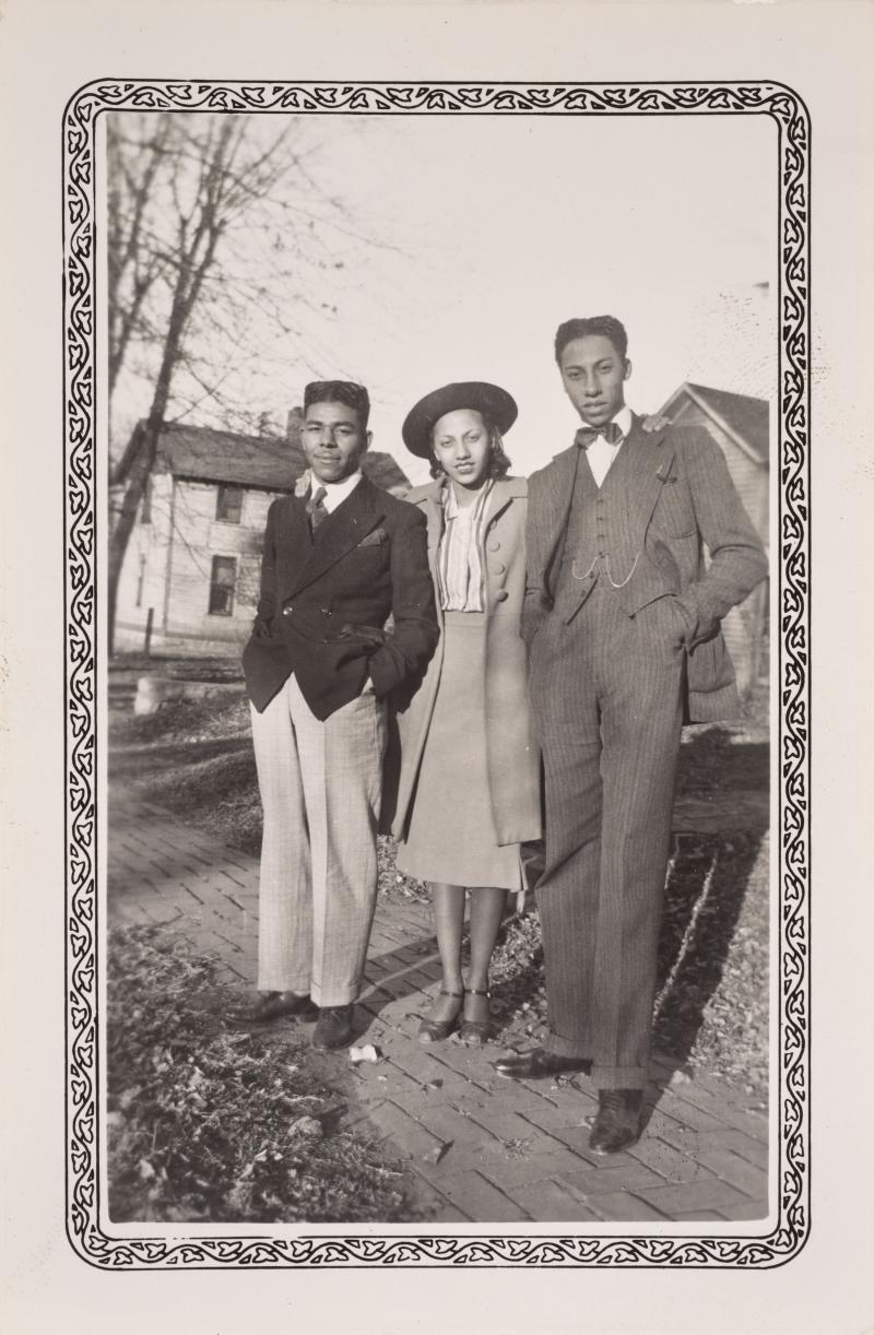 three people, 2 men with a woman between them photographed outside