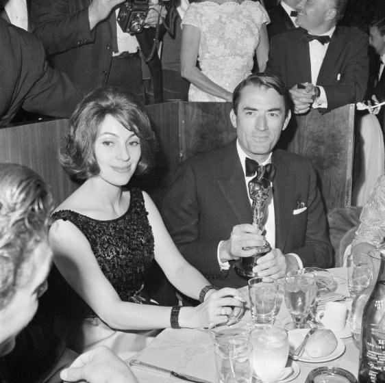 Black and white photo of Véronique and Gregory seated next to each other at a table in glamorous attire.