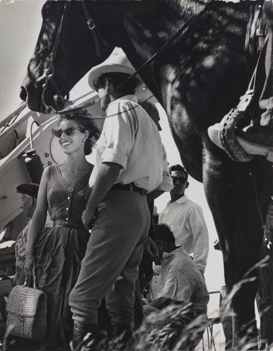 Black and white photograph. A horse in the foreground and Véronique and Gregory talking in the background.
