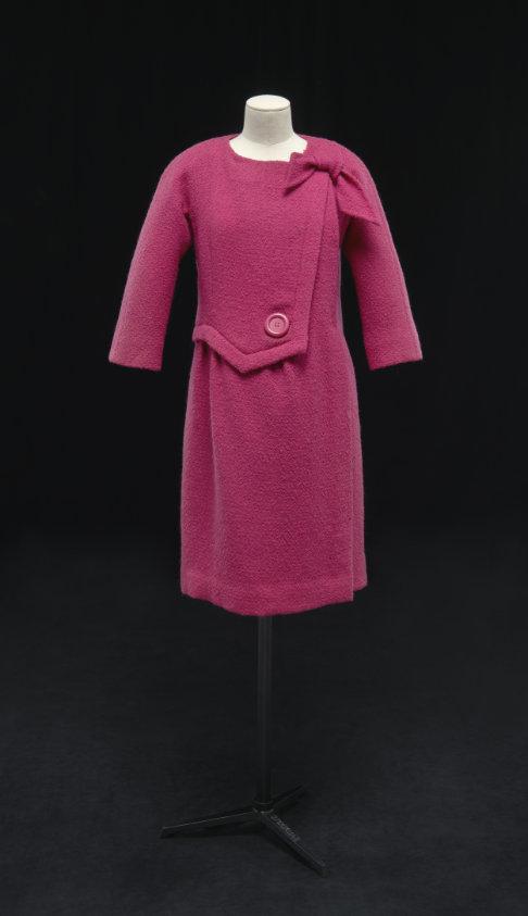 Long sleeve and knee length magenta pink coatdress. Large button at the waist and bow on the left shoulder.