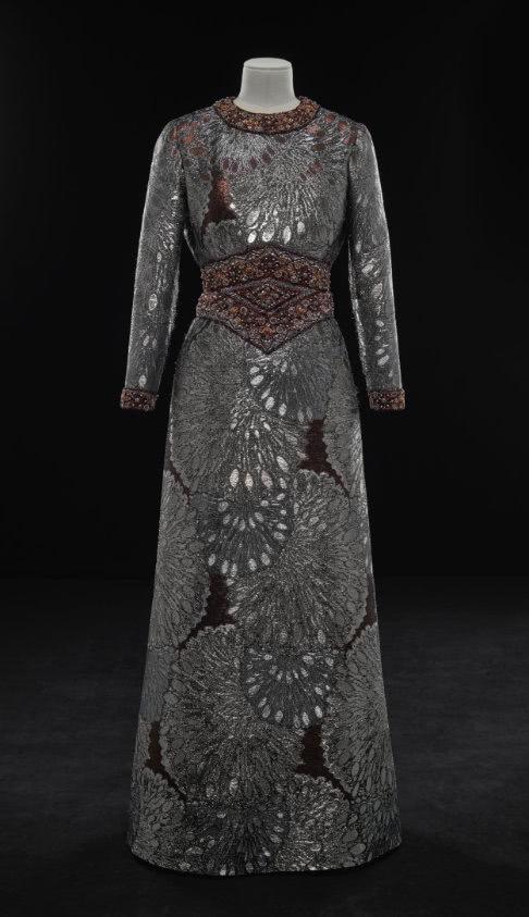 Dark long sleeve and floor length dress. Detailed beading at the neck and waist, with an overall large floral pattern.