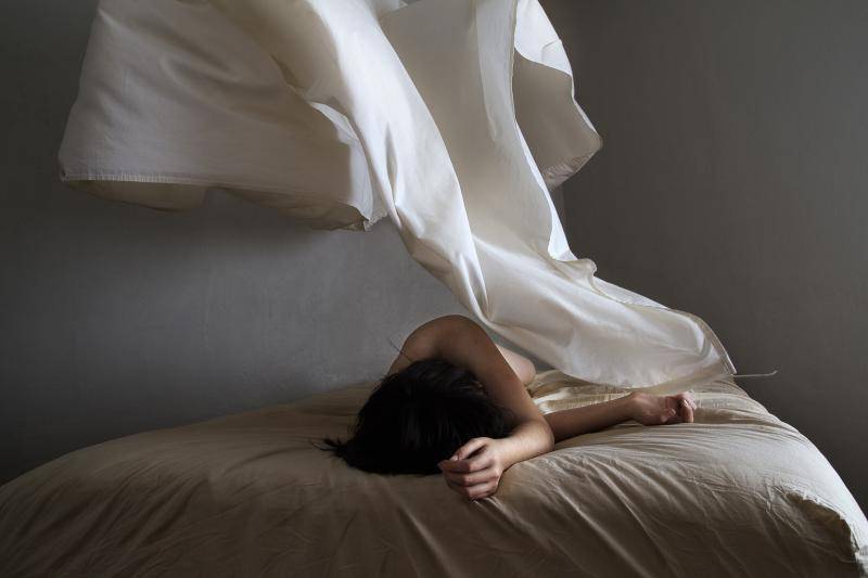 Fotografía de una mujer de vestido blanco recostada sobre una cama