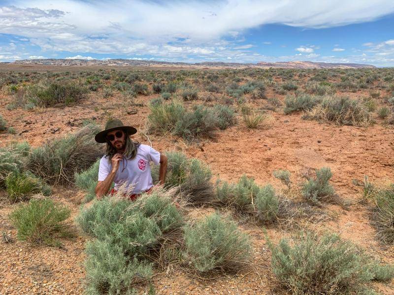 Kevin Philip Williams wears a hat and is sitting in a landscape in Utah with wild Artemisia plants