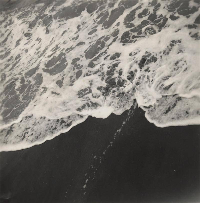 Black and white photograph of the tide rolling up on a black sand beach