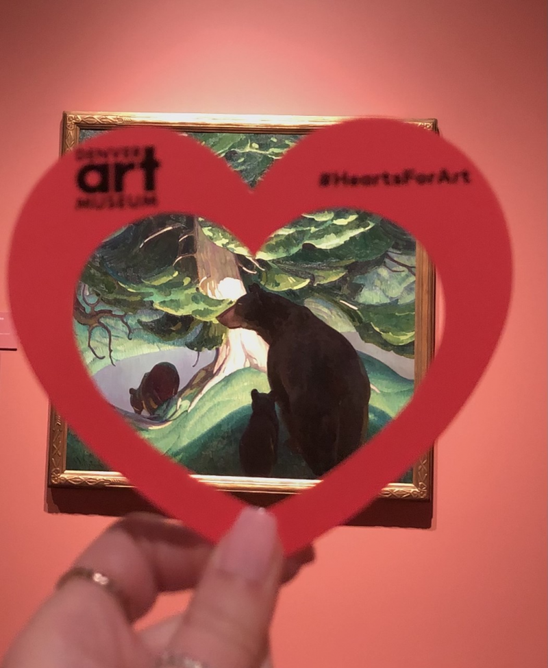 Hand holding a paper heart in front of the artwork "Black Bears" by Herbert Dunton at the Denver Art Museum.