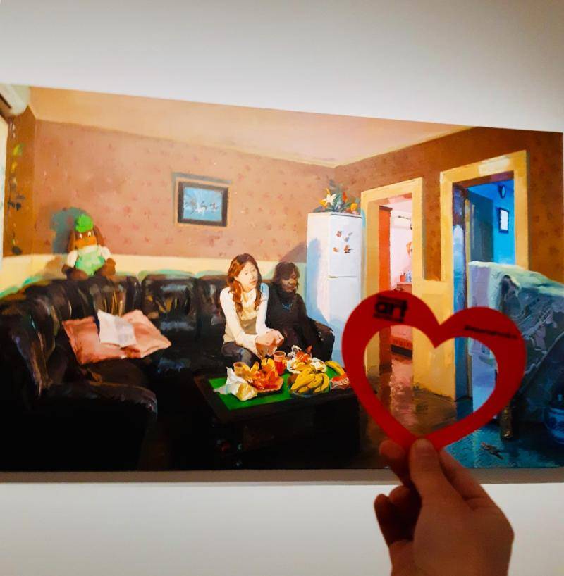 Hand holding a paper heart in front of the artwork, "She—White Collar Worker" by Yu Hong