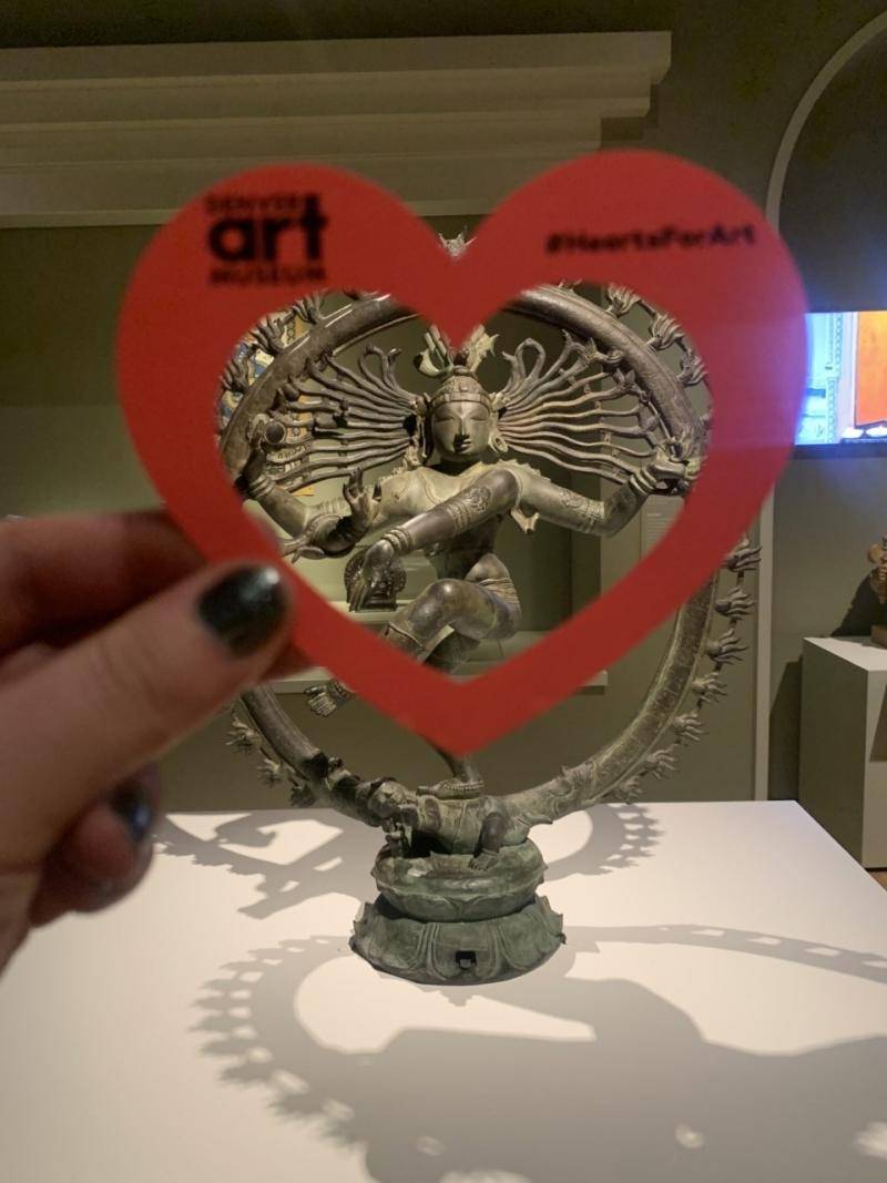 Hand holding a paper heart in front of the statue "Shiva Nataraja"
