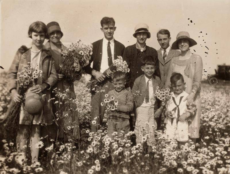Family of adults and children from the 1920s posing together in a flower garden