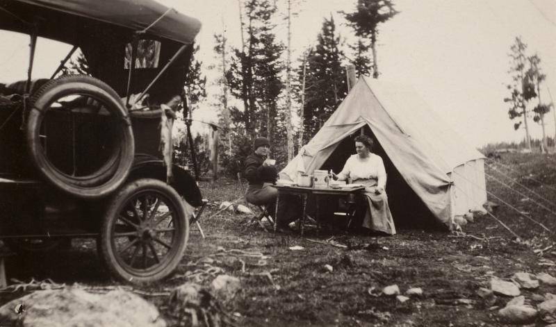 Old photograph of a woman sitting and writing outside in front of a tent