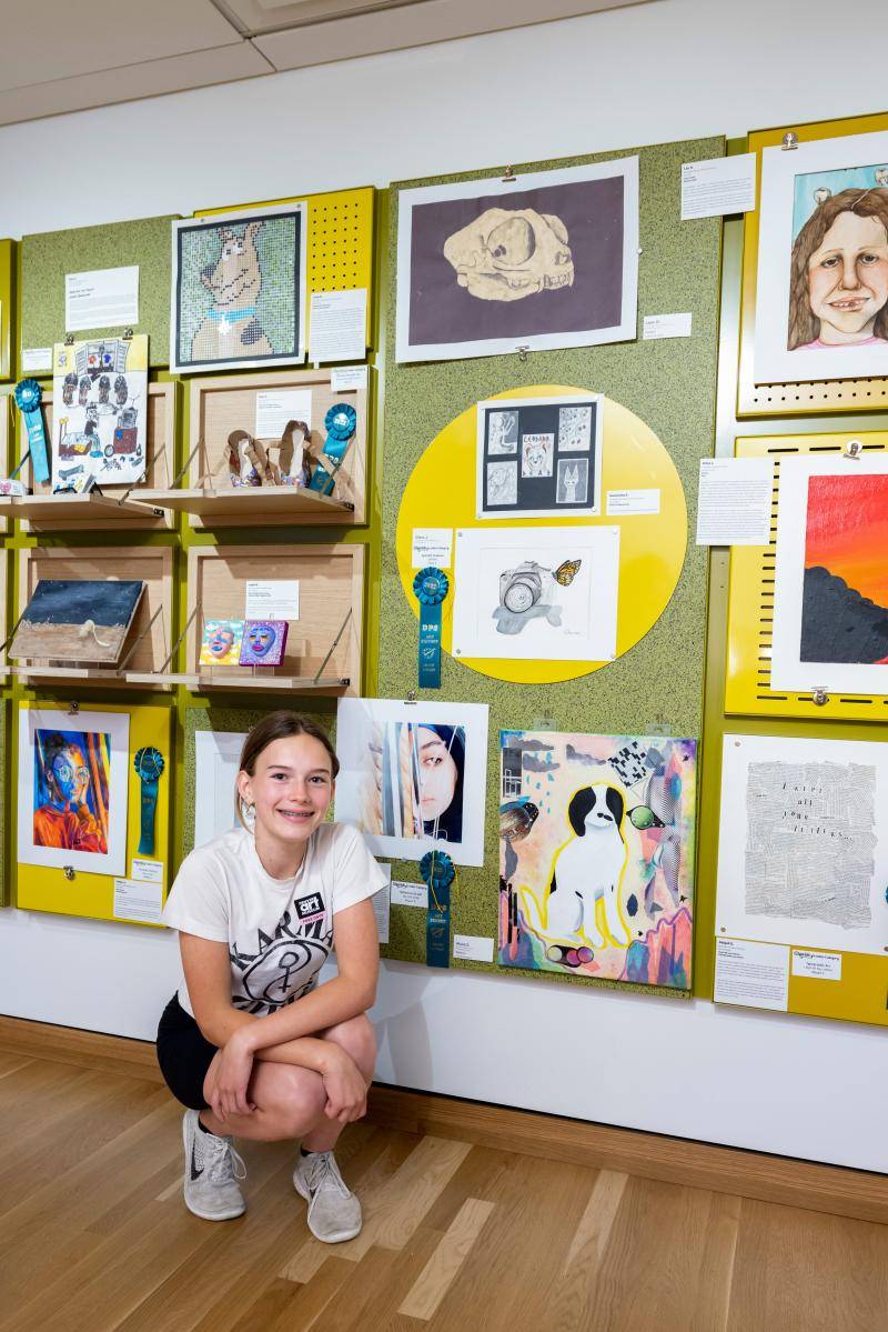 Student posing in front of their artwork on display in the showcase