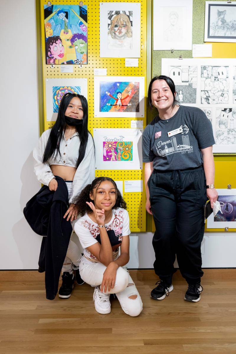 Students posing in front of their artworks on display in the showcase