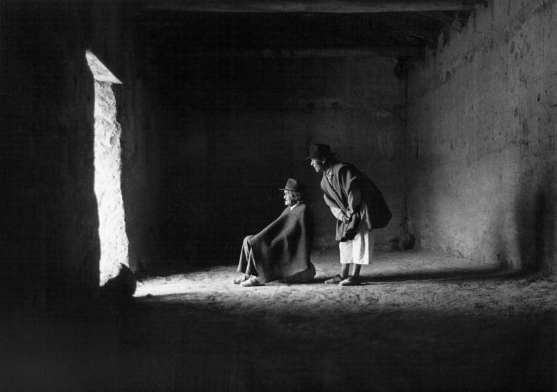 Black and white photograph of two people in a room looking out to the sunlight