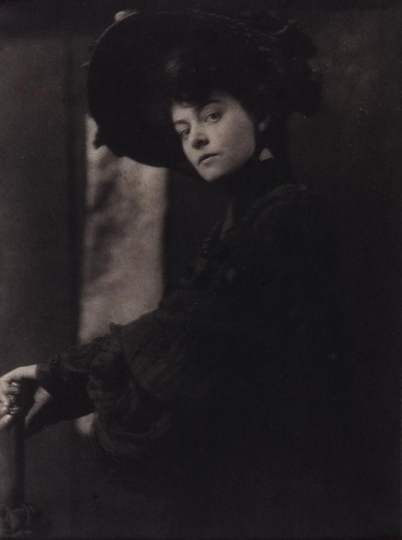 Black and white photograph of a young woman dressed in a black formal dress and hat