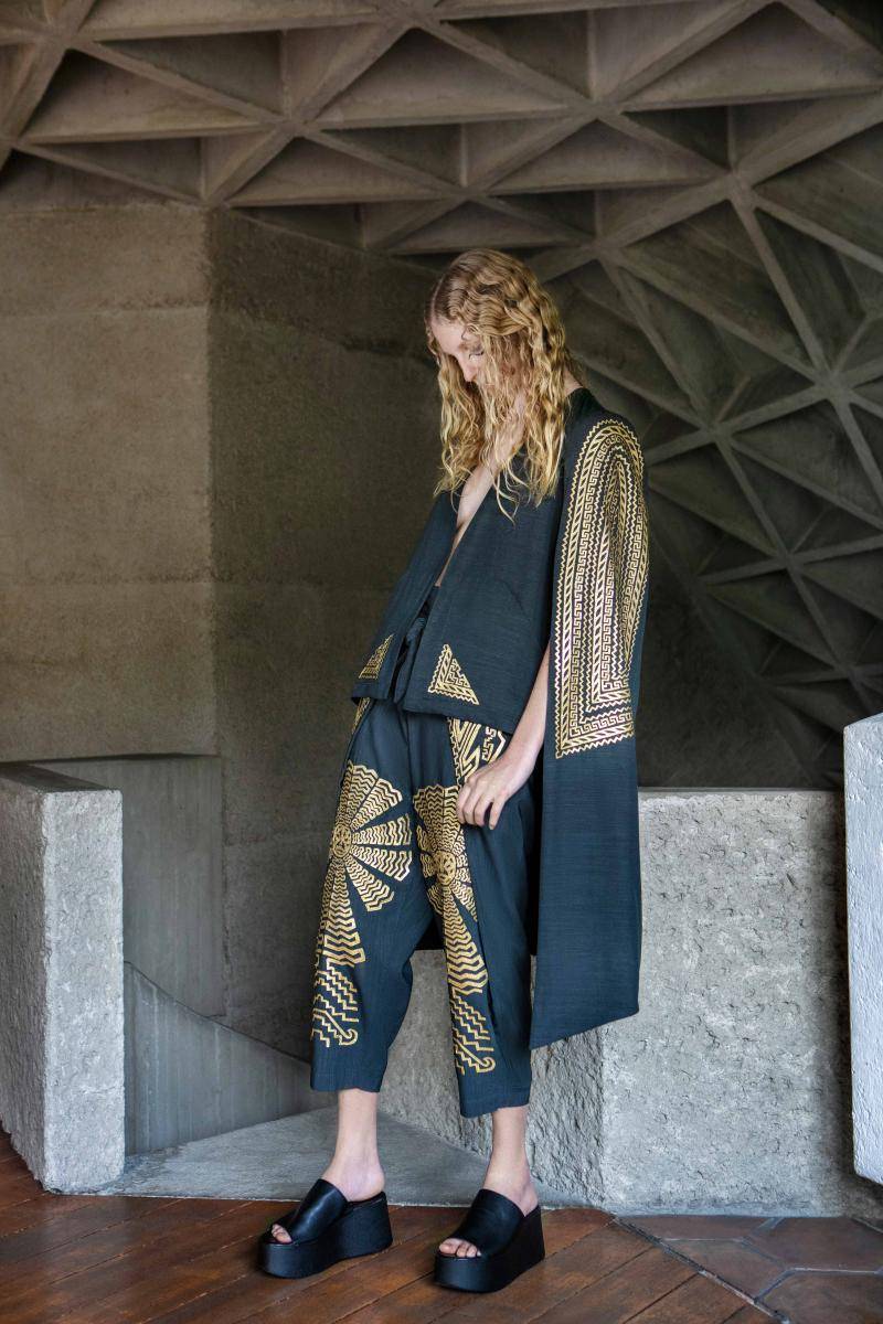 Model wearing deep blue/green clothing with cape and gold patterns