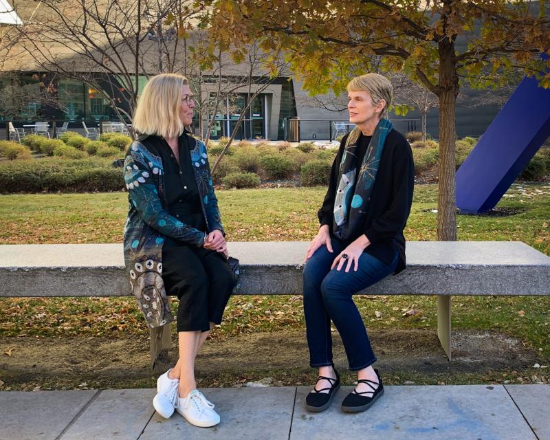 two women sit on a bench outside the museum modeling a duster and a scarf by Betsy Wiersma