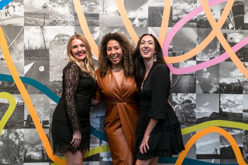 Three women posing in front of a mural