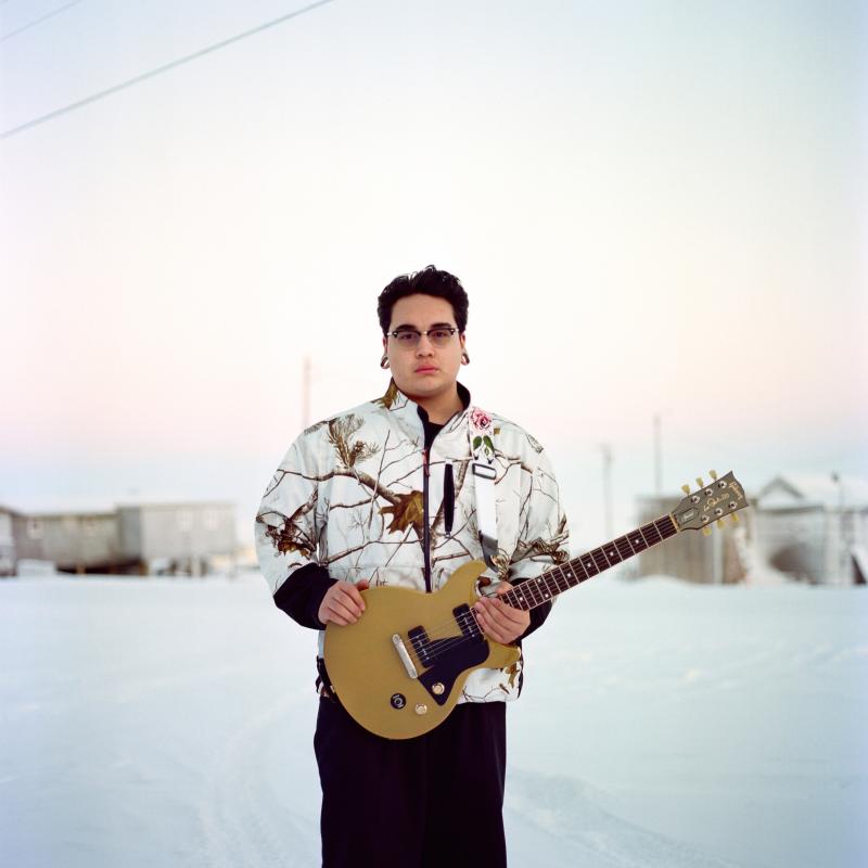 Inuit man posing in a snowy Alaska landscape holding his guitar