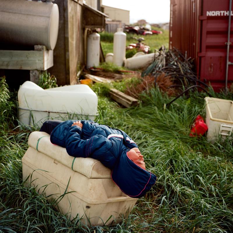 Photograph of construction site with a young girl in a blue jacket lying down and looking up