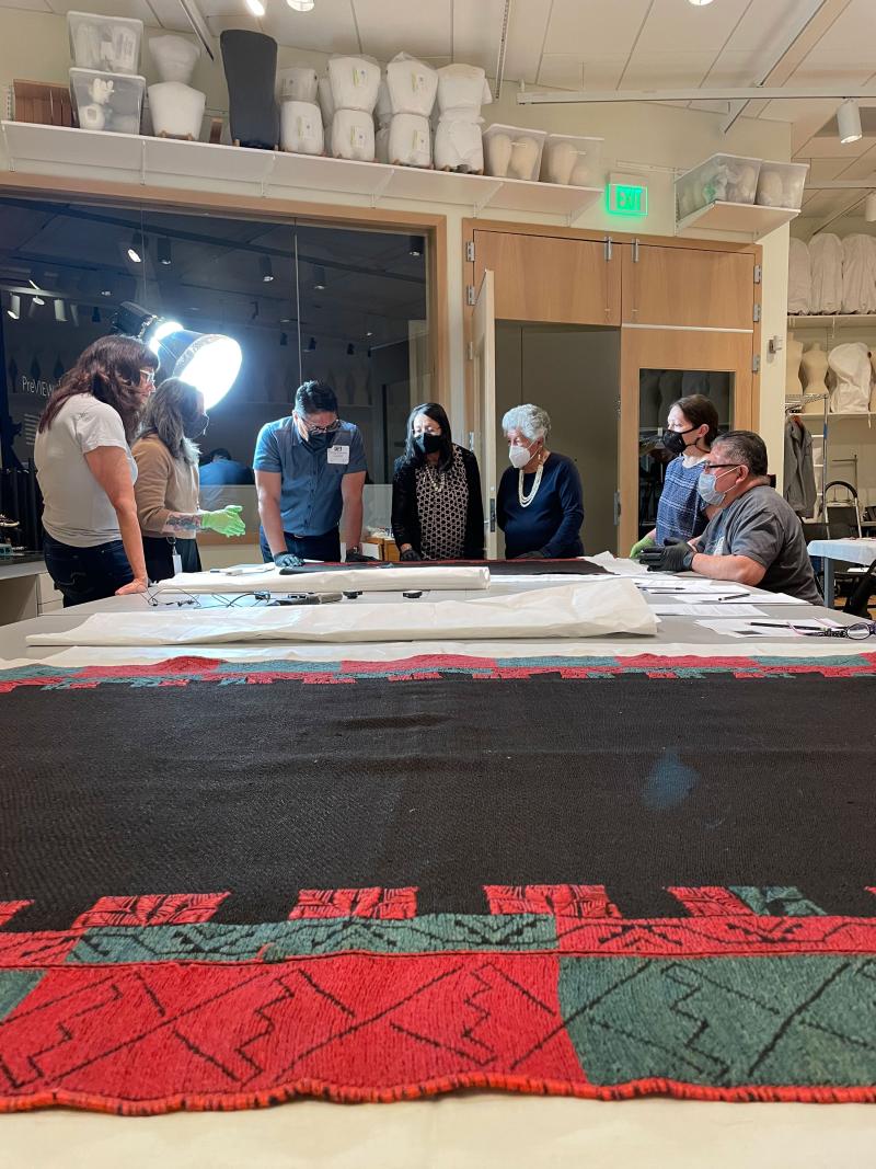 DAM staff and Acoma cultural advisors looking at a large cloth on a table in the textile conservation lab