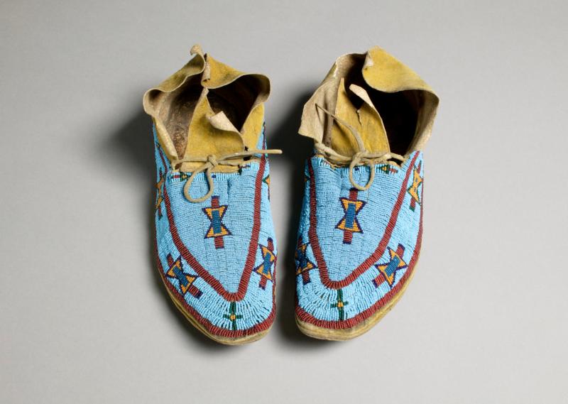 Moccasins made out of leather and beads with a bright blue patterned coloring on the outside