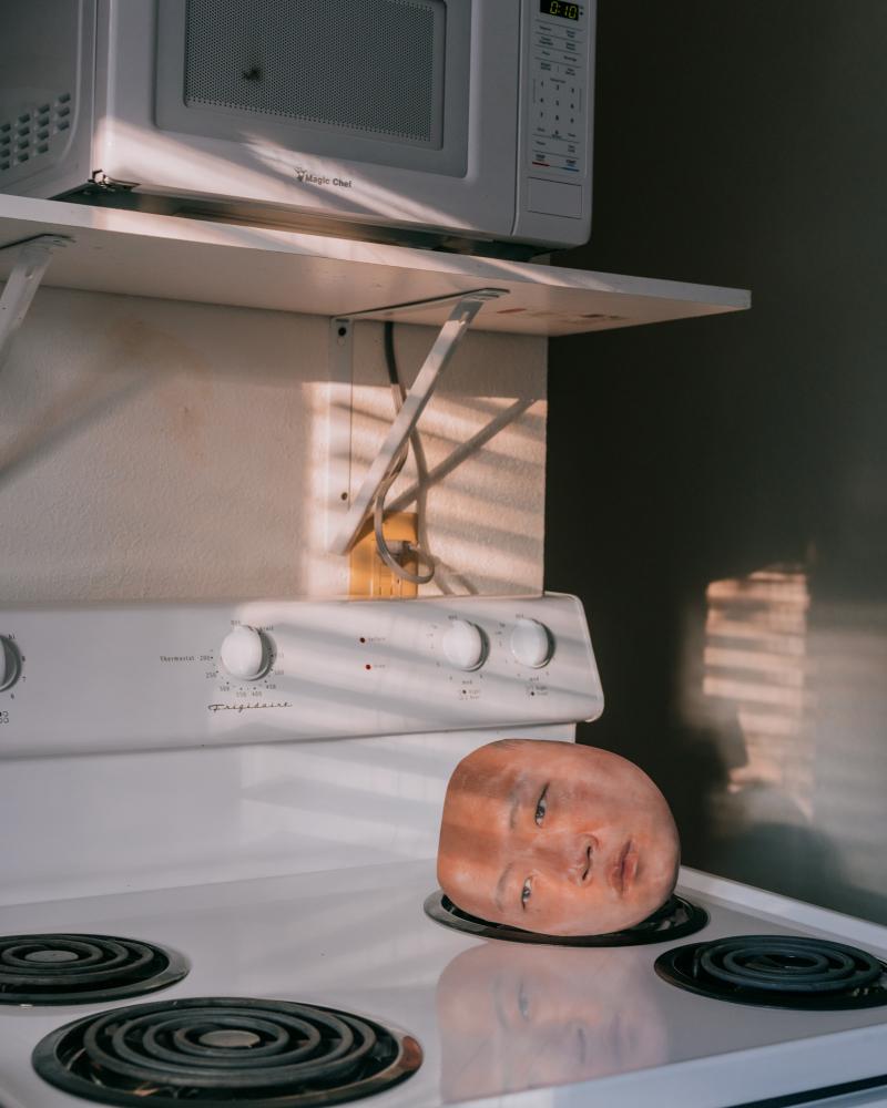 Surreal photograph of severed head resting on a kitchen stovetop