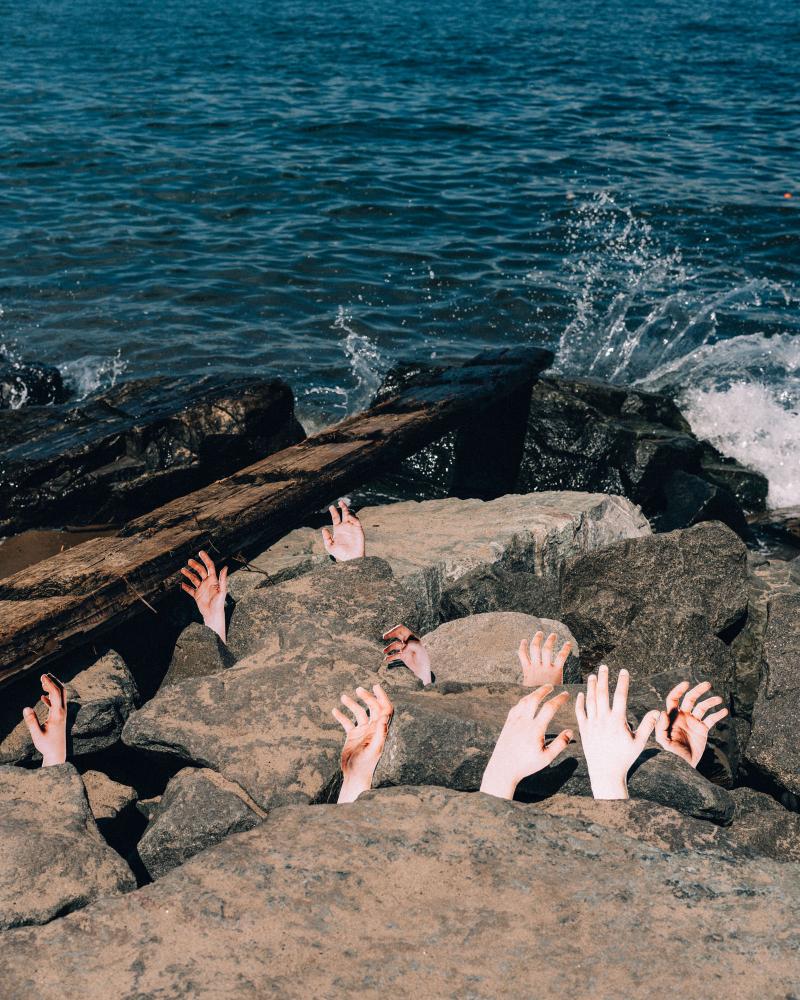 Severed hands rising from the rocks near a beach and body of water