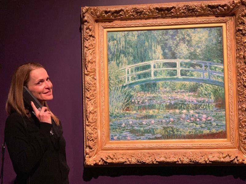 Woman listening to audio guide in front of a painting of the Japanese bridge in the Monet exhibition